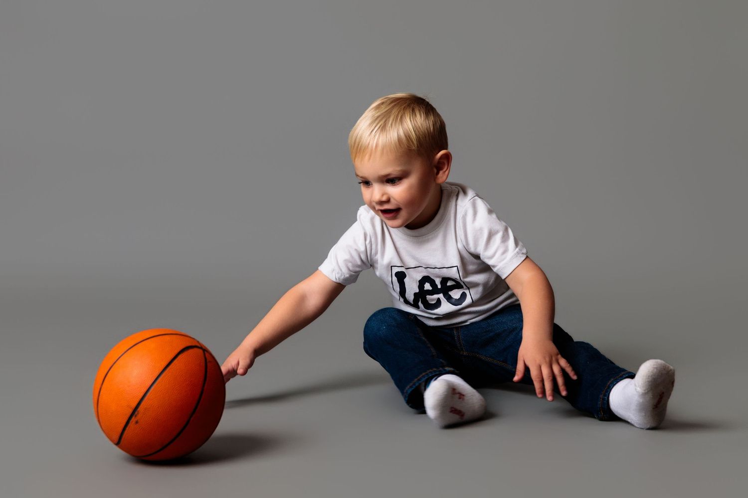 Action shots of child playing with basketball showing movement and energy against grey backdrop.