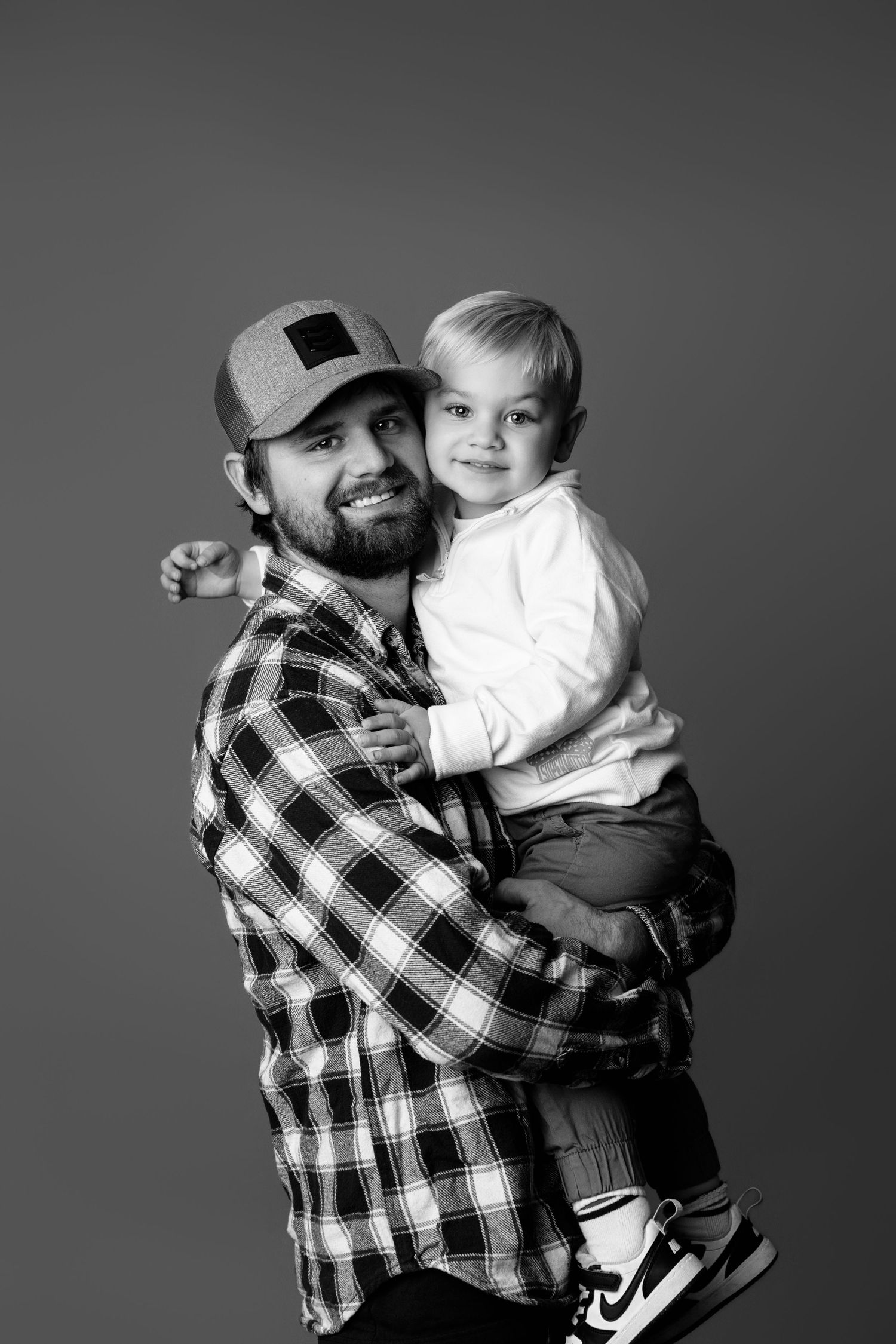 Playful studio portraits showing adult and child in matching plaid shirts against grey background.