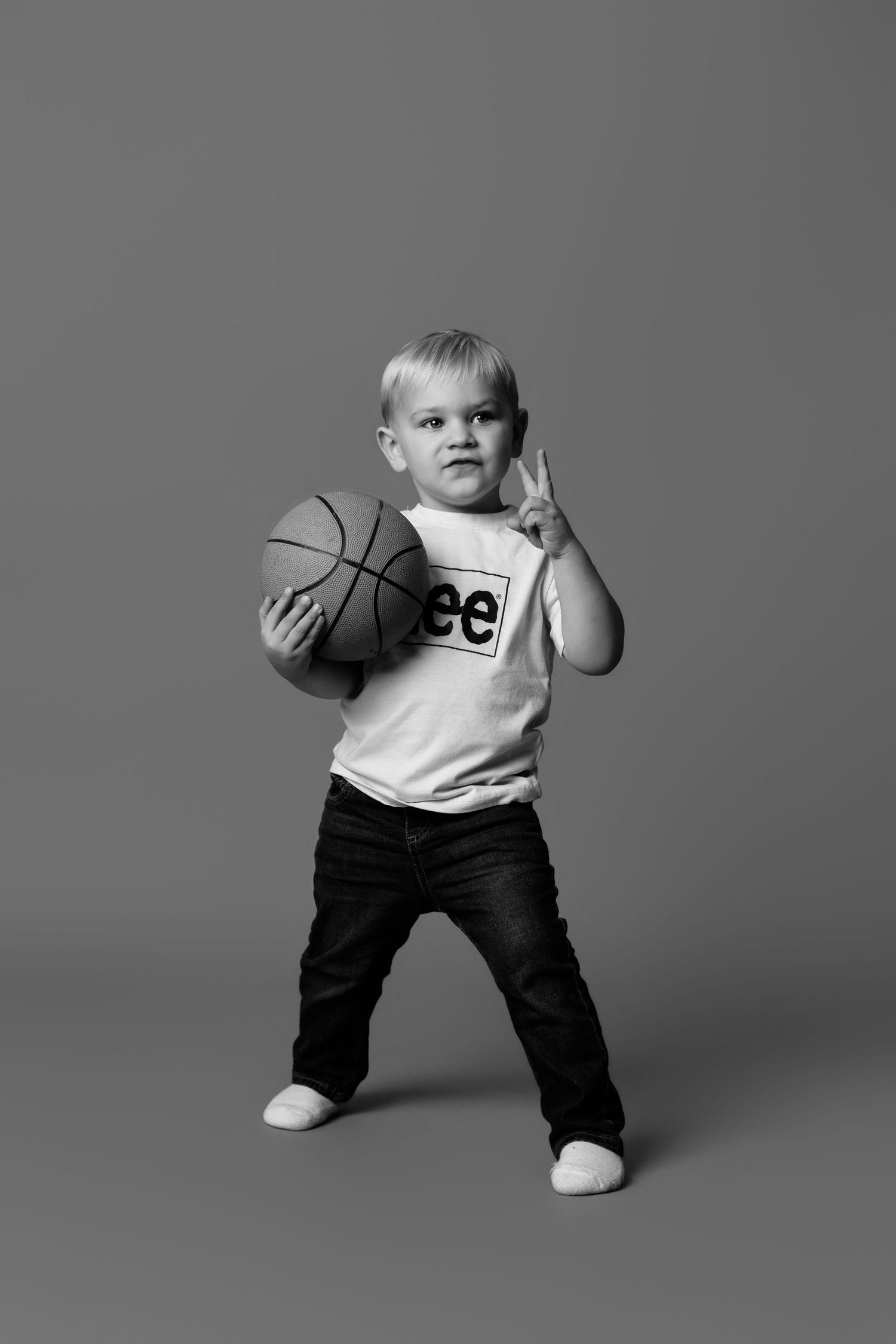 Black and white photo series showing a young child in casual wear striking different playful poses with a basketball.