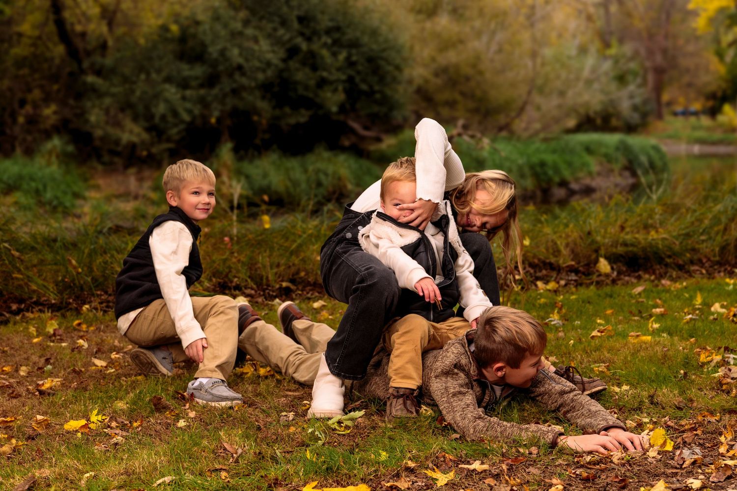 Three people playing in fallen autumn leaves near a pond on a sunny fall day.