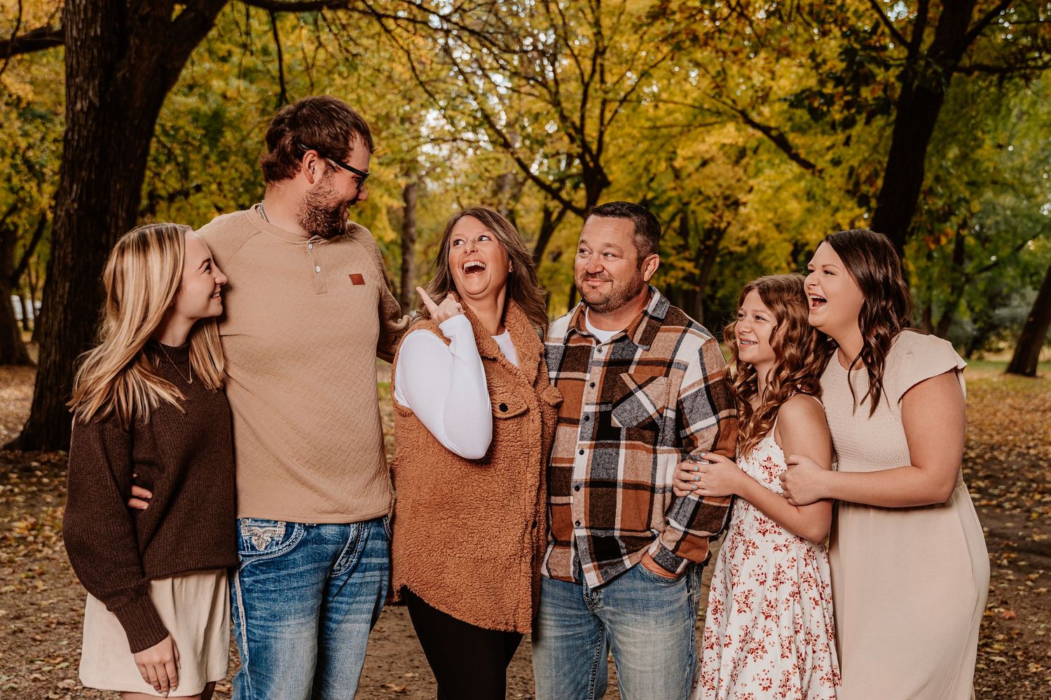 People share joyful laughter while standing together in a wooded autumn setting.