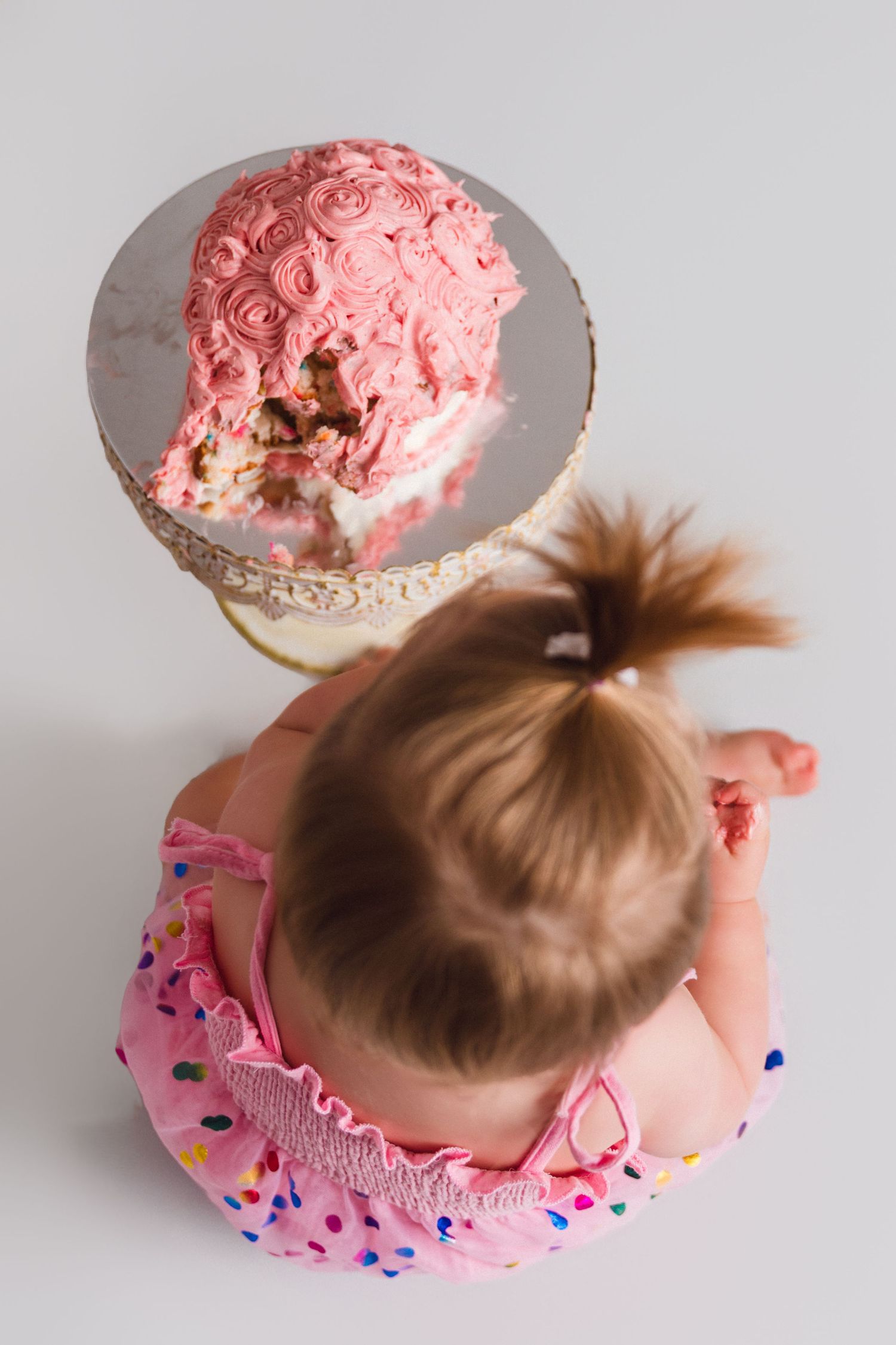 Overhead view of baby diving into pink frosted cake during cake smash photo session.