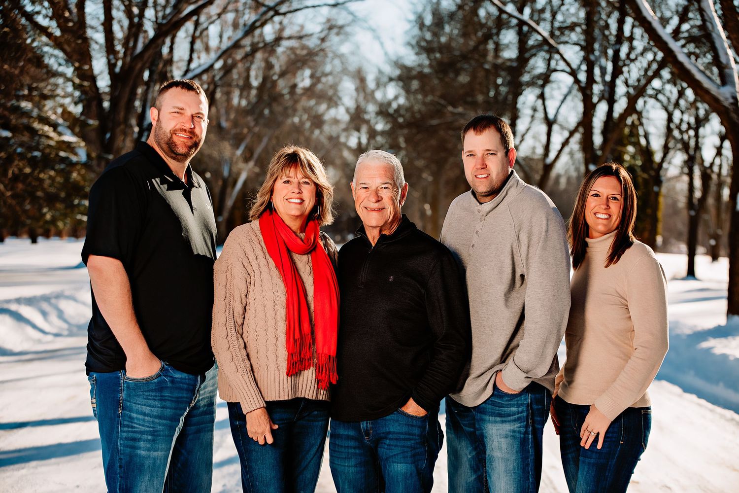 A family of five poses together on a snow-covered path with winter trees behind them.