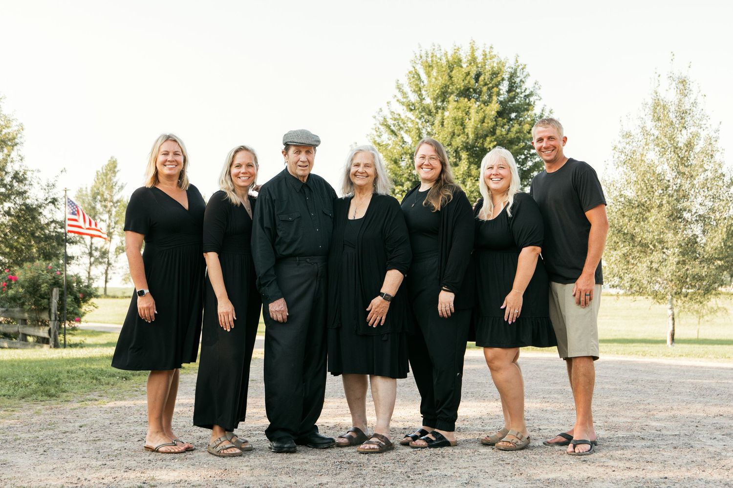 A large group wearing coordinated black outfits poses together outside on a sunny day.