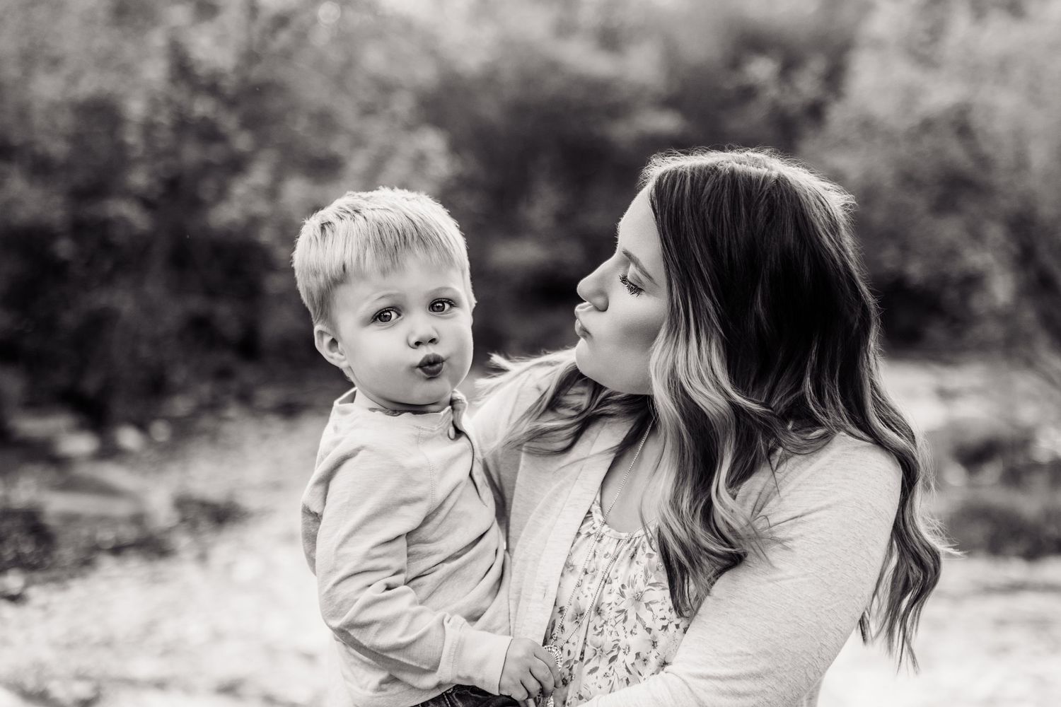 Black and white photo of a young mother holding her toddler son outdoors, sharing a tender moment.
