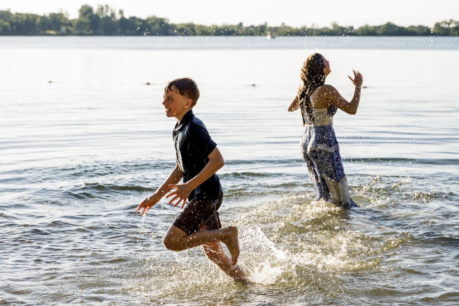 Boy and girl running and splashing through shallow lake water on a bright sunny day.