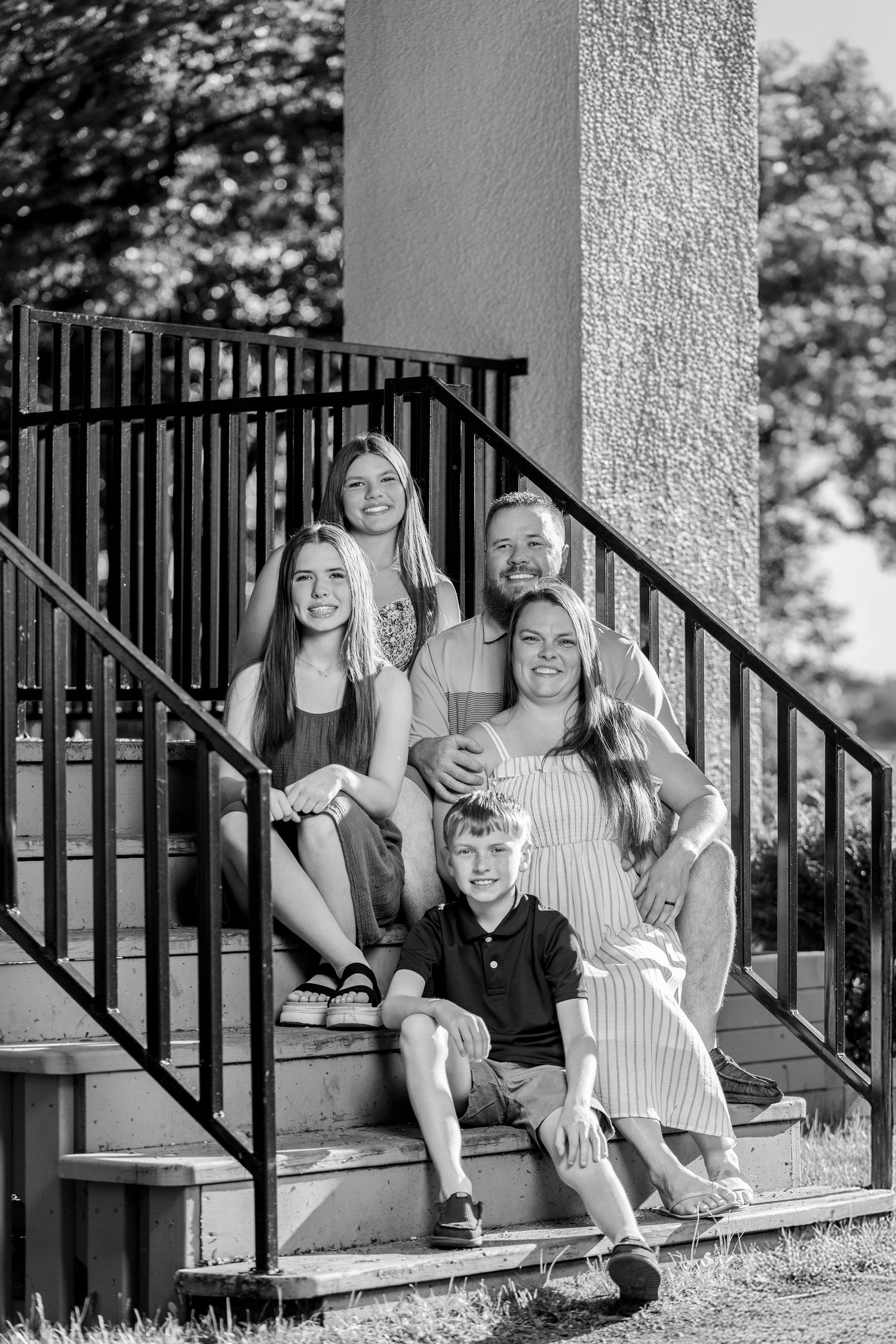 Black and white family portrait of five people sitting on outdoor steps near iron railing.