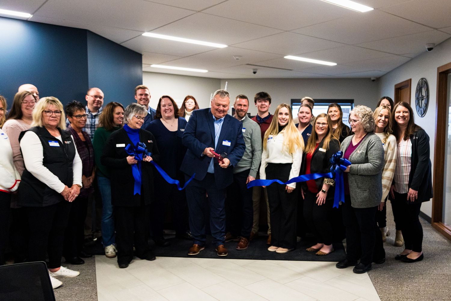 Group of professionals celebrating a ribbon cutting ceremony in a modern office space with blue decor.