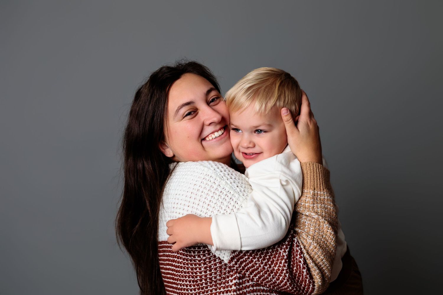 Warm embrace between parent and child in black and white portrait against grey background.