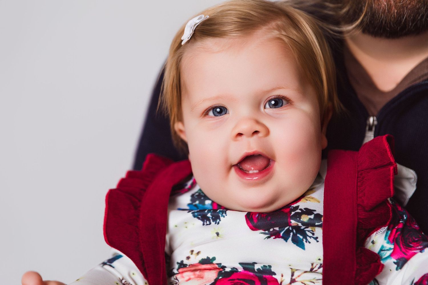 Close up of a smiling baby wearing a red and white floral dress with a hair bow.