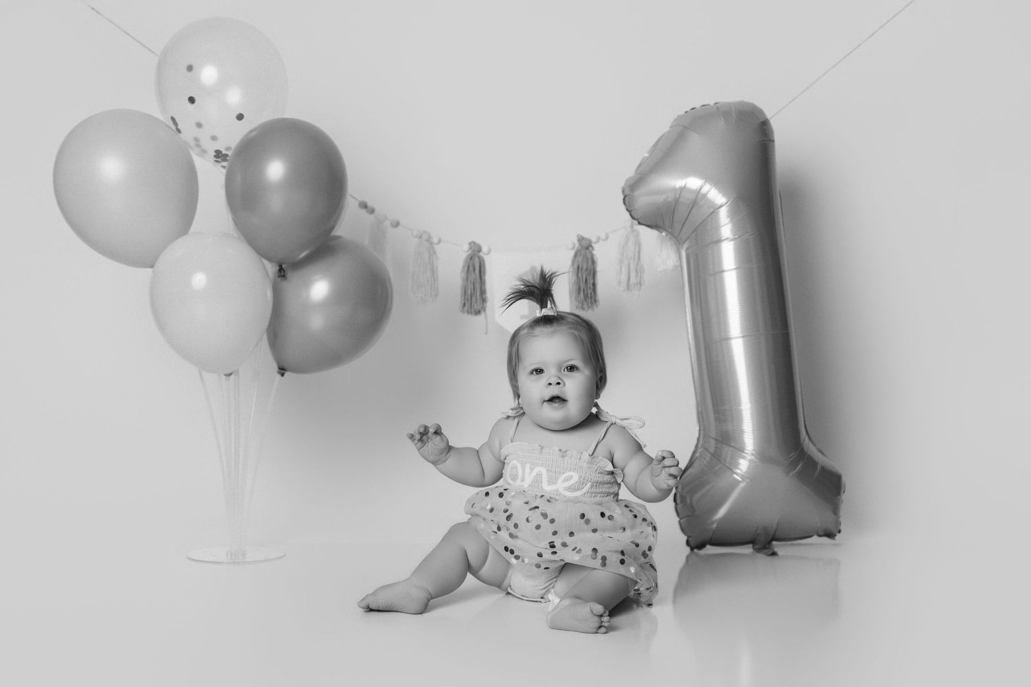 First birthday celebration setup with silver and white balloons against light background.
