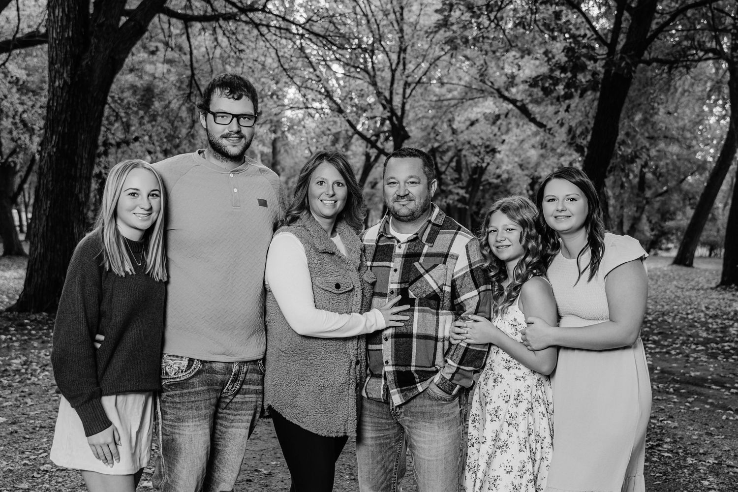 Black and white portrait of a group standing together in a wooded park setting during fall.