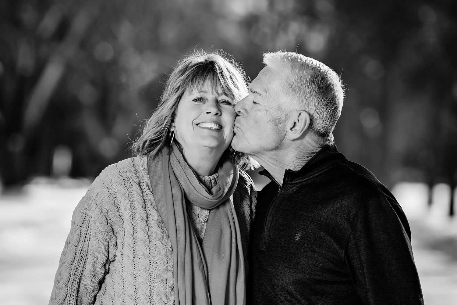 A tender black and white portrait of a couple sharing an affectionate moment outdoors.