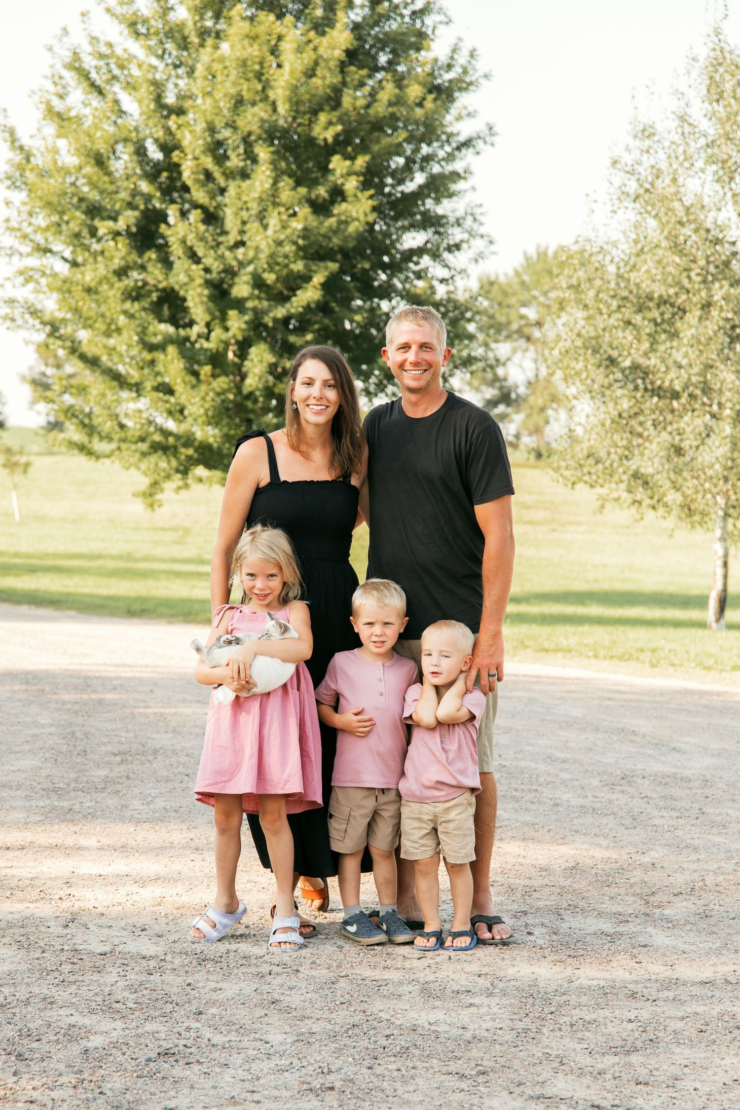 A family wearing coordinated pink and black outfits poses together outdoors in a park setting.