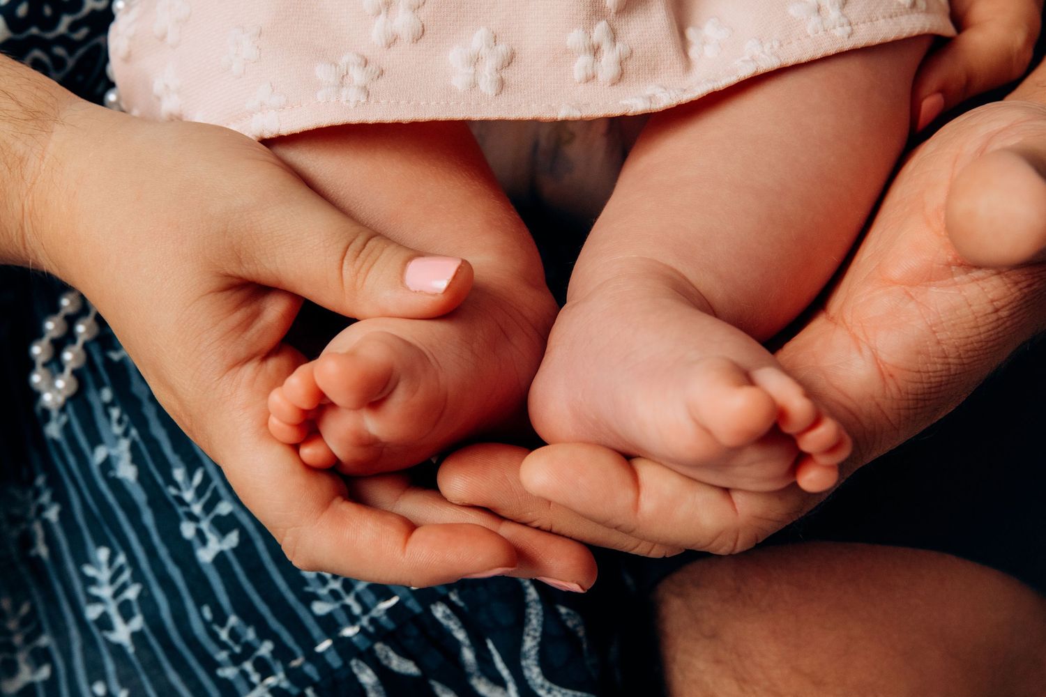 Tiny baby feet resting in gentle adult hands on blue patterned fabric.