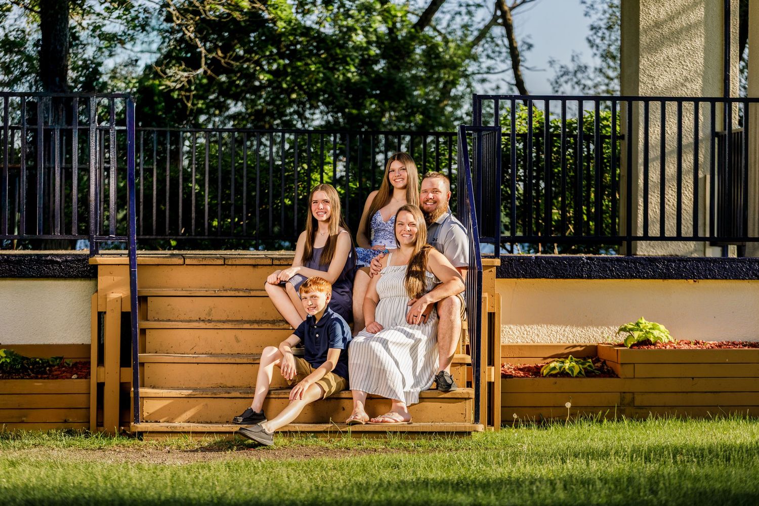 Happy family of five posing on wooden deck steps outdoors on sunny day.