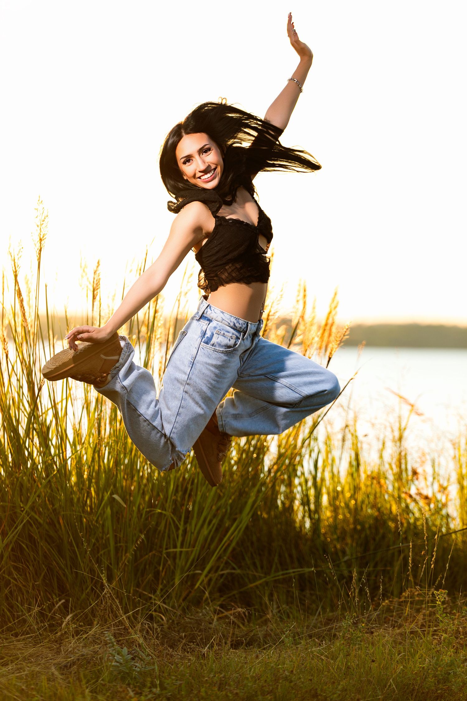 A person in jeans leaps gracefully through tall grass at sunset, creating a dynamic silhouette against the golden sky.