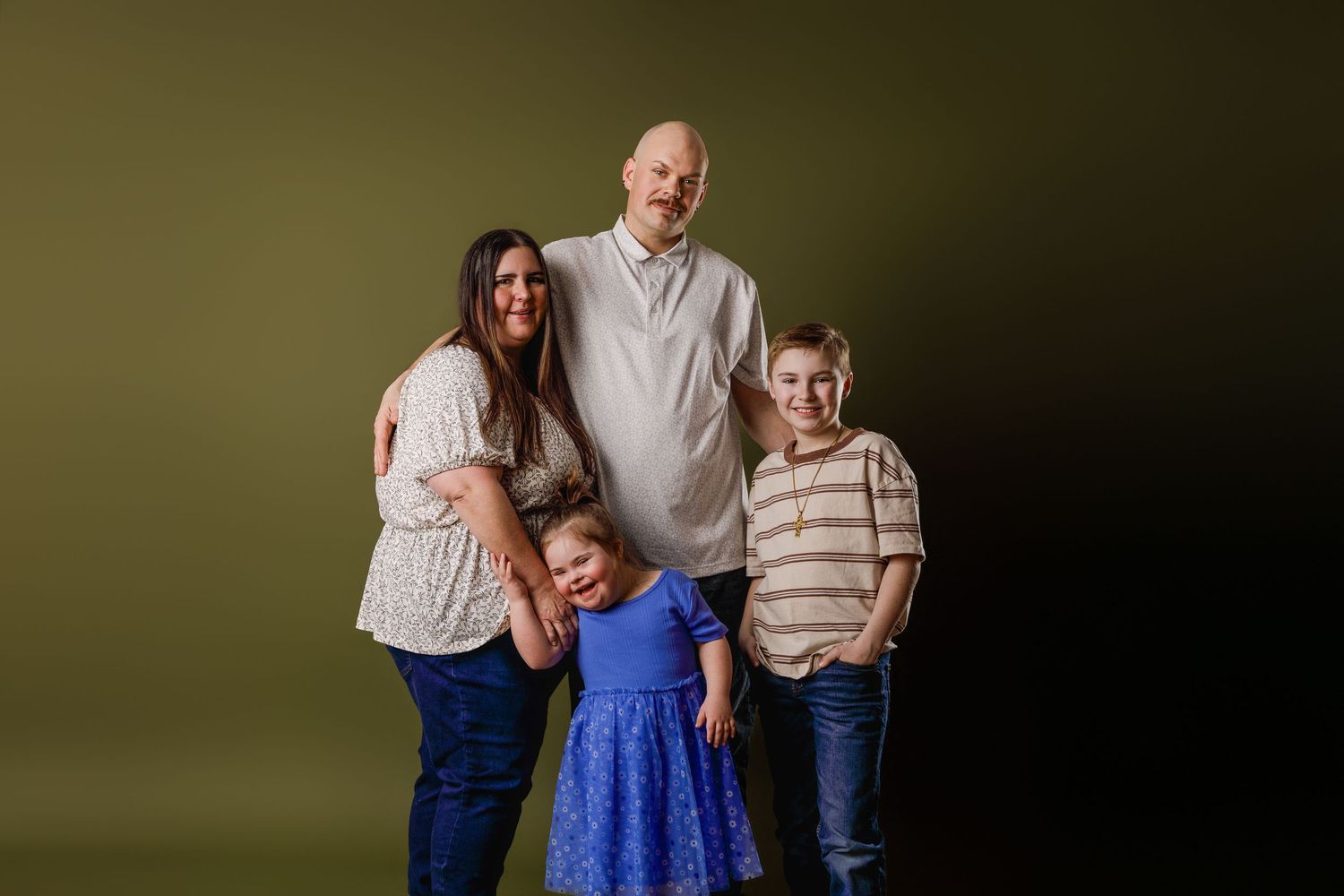 Family of four posing for a studio portrait against an olive green background, including two parents and two children.