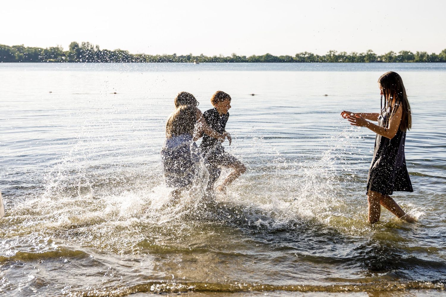 Three kids laughing and splashing each other in a lake while a girl watches during family photos.
