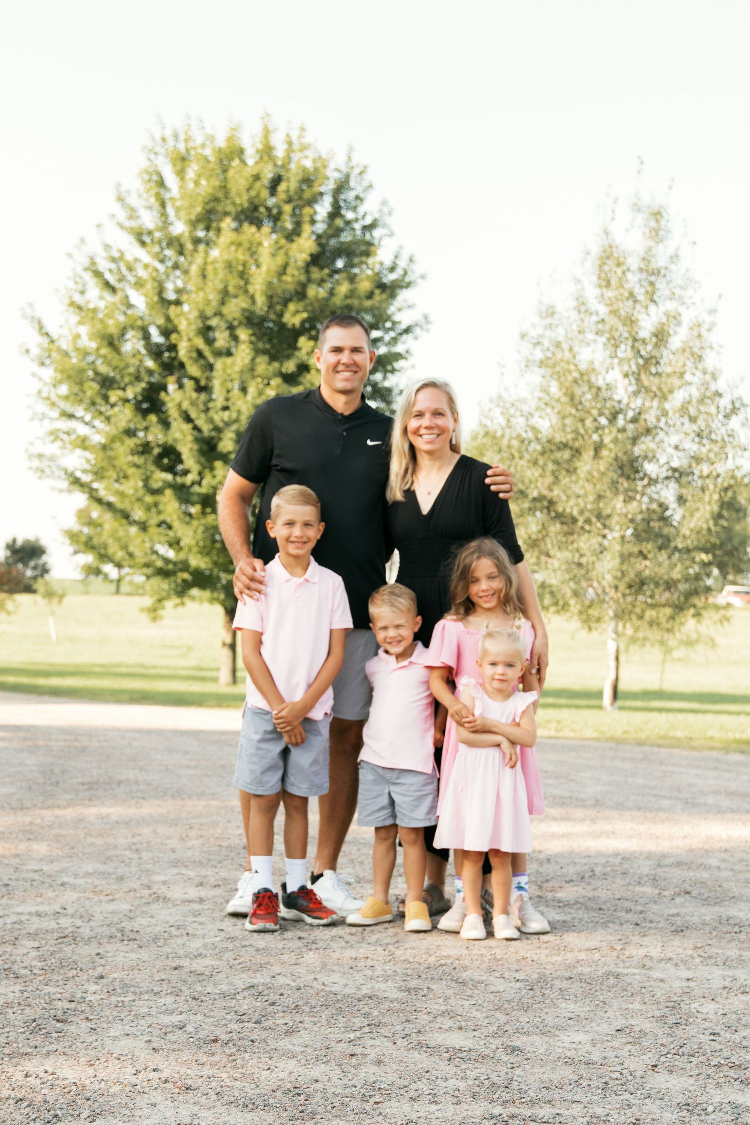 A family group stands together for portraits in casual summer clothing on a sunny day outdoors.