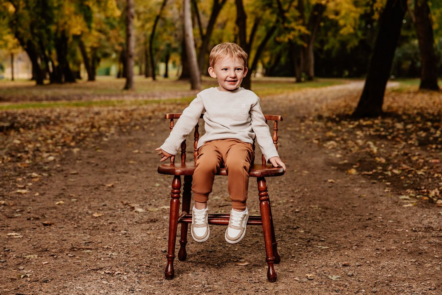 Small child sits in vintage wooden chair during autumn outdoor photo session.
