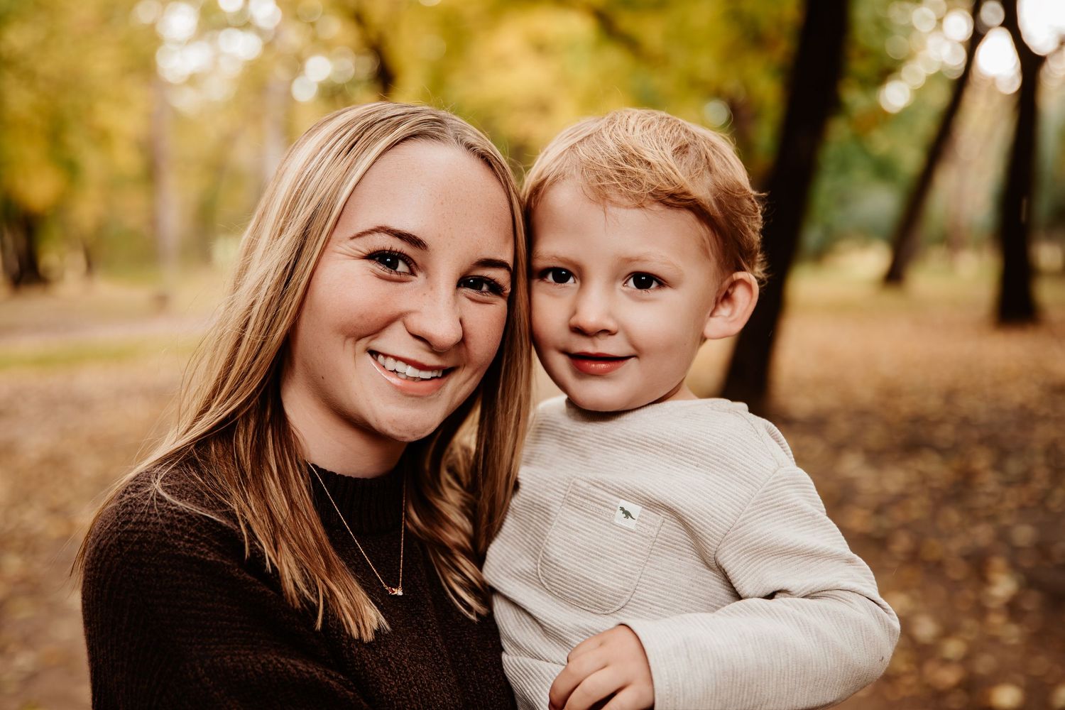 A tender autumn portrait of parent and child embracing outdoors among fall trees.