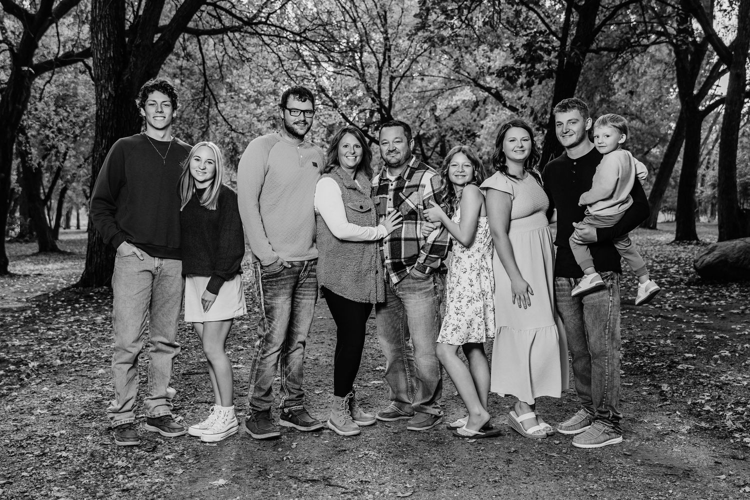 Black and white outdoor portrait of a group of people standing together in a park setting among trees.