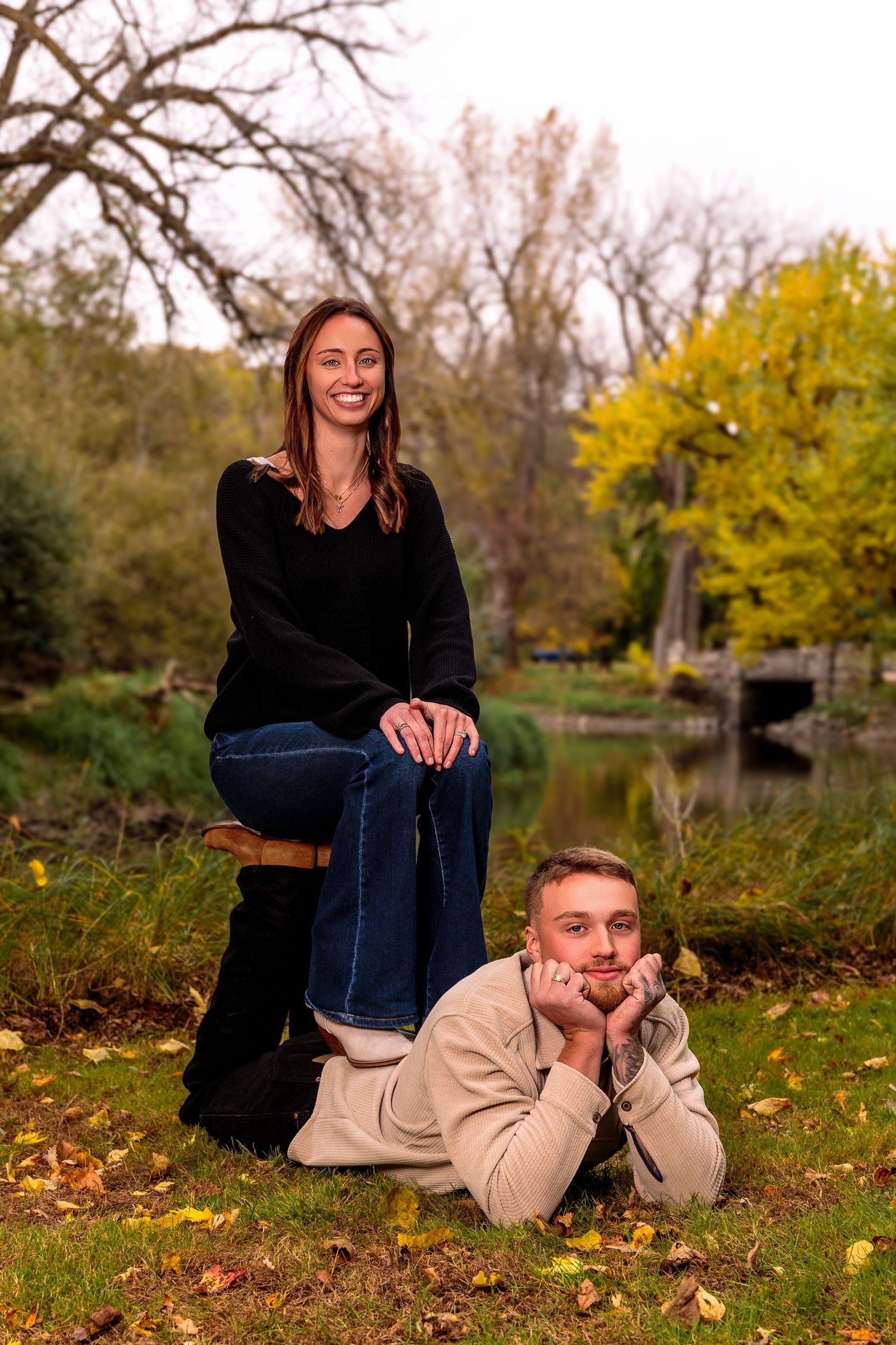Casual outdoor photo session with couple laying on autumn leaves near a pond.
