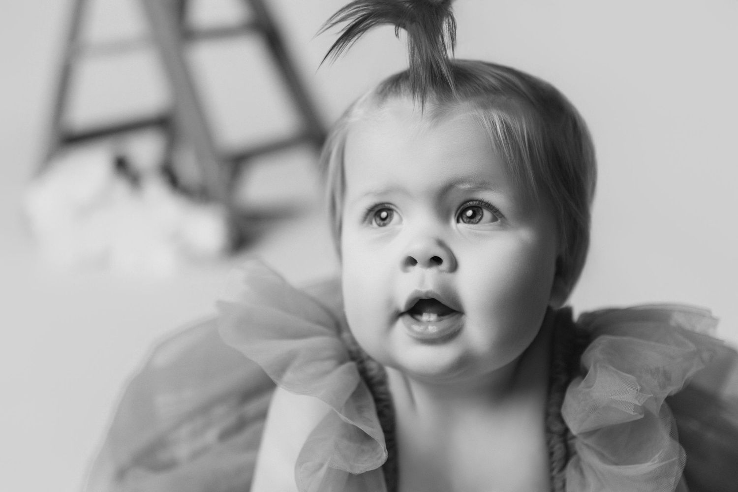 Baby with spiky hair poses near wooden ladder during studio photoshoot.