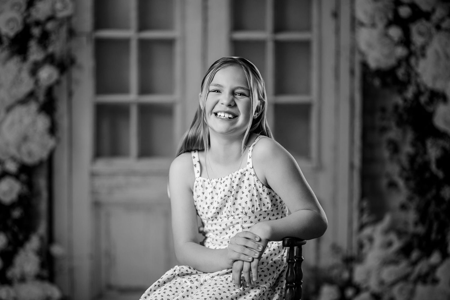 Happy young girl in polka dot dress laughing while seated in black and white portrait photo.