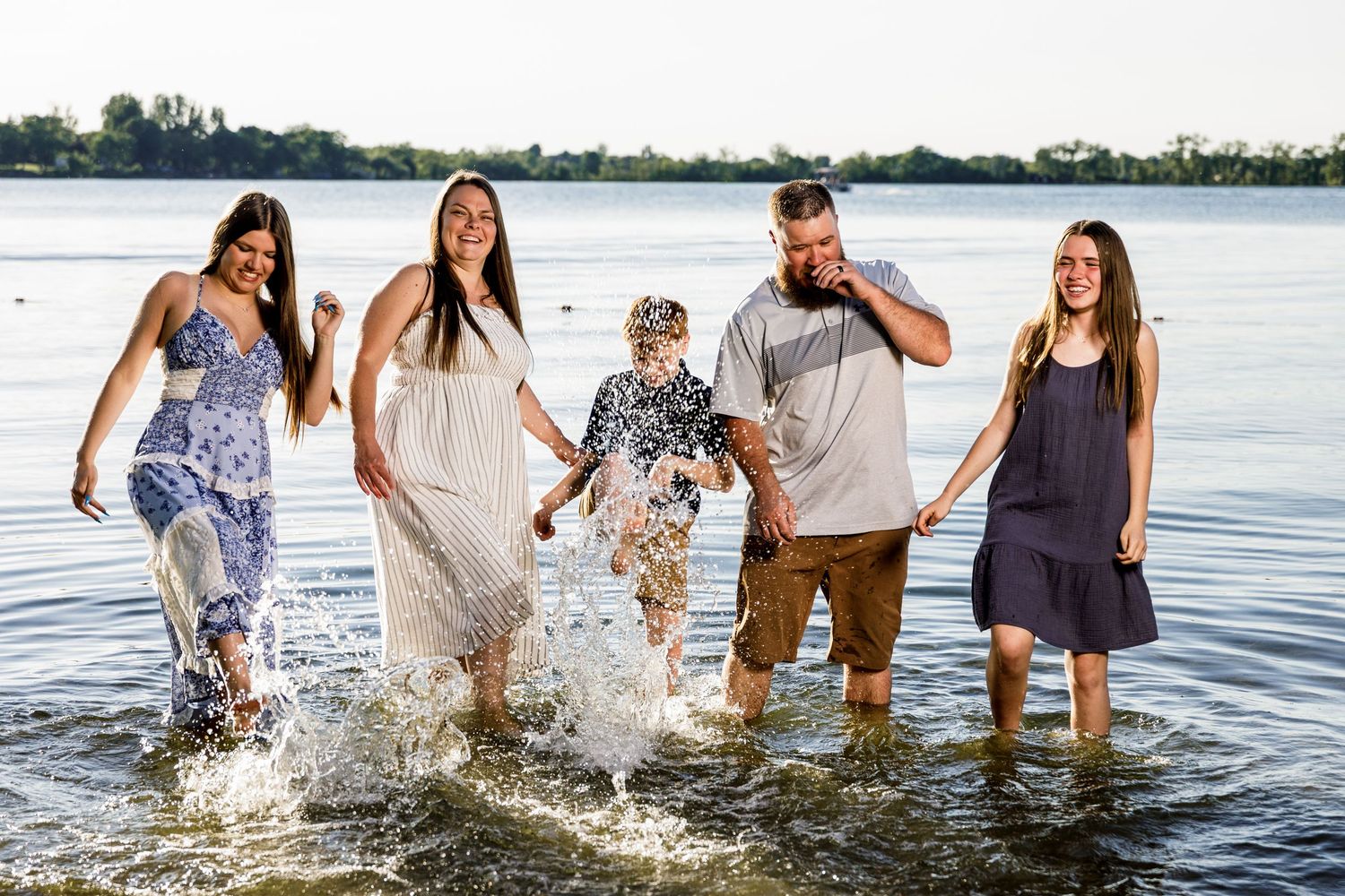 Joyful family of five splashing and playing together in a lake at sunset.