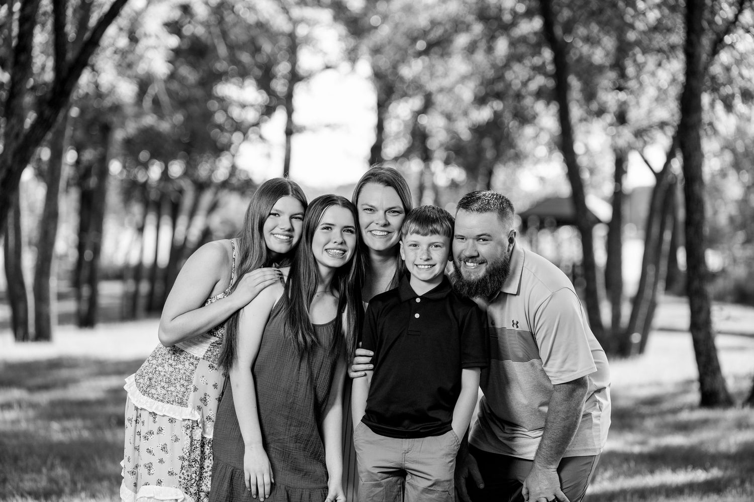 Black and white family portrait of five people smiling outdoors among trees.