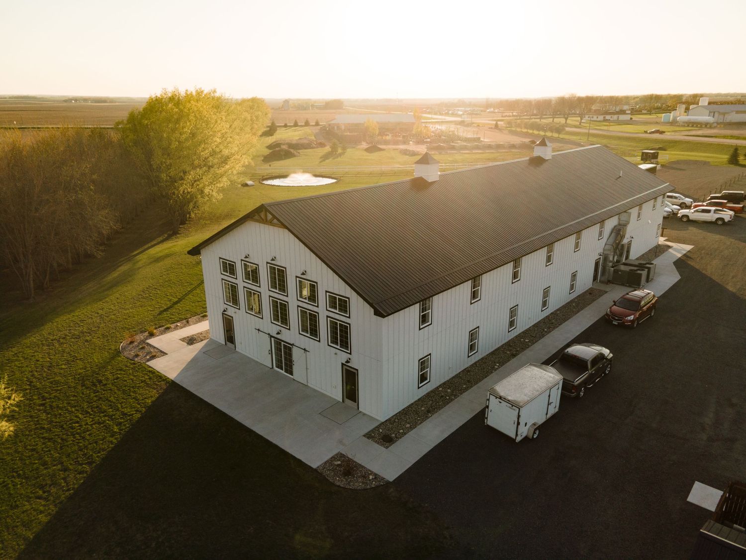 Aerial drone view of a large white commercial building with multiple entrances and a parking lot at sunset.