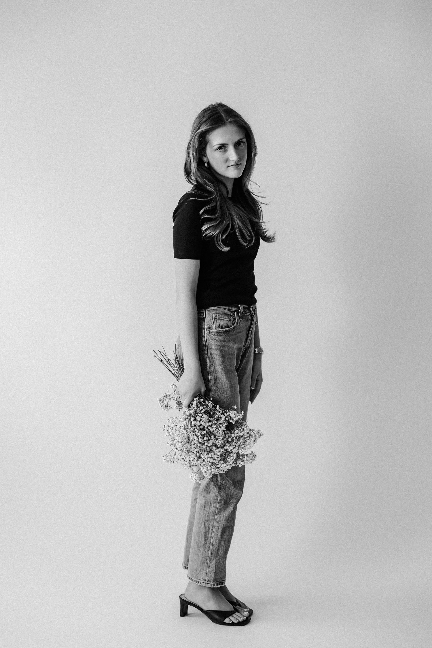 Young woman standing in profile holding wildflowers, black t-shirt and jeans, black and white photo.