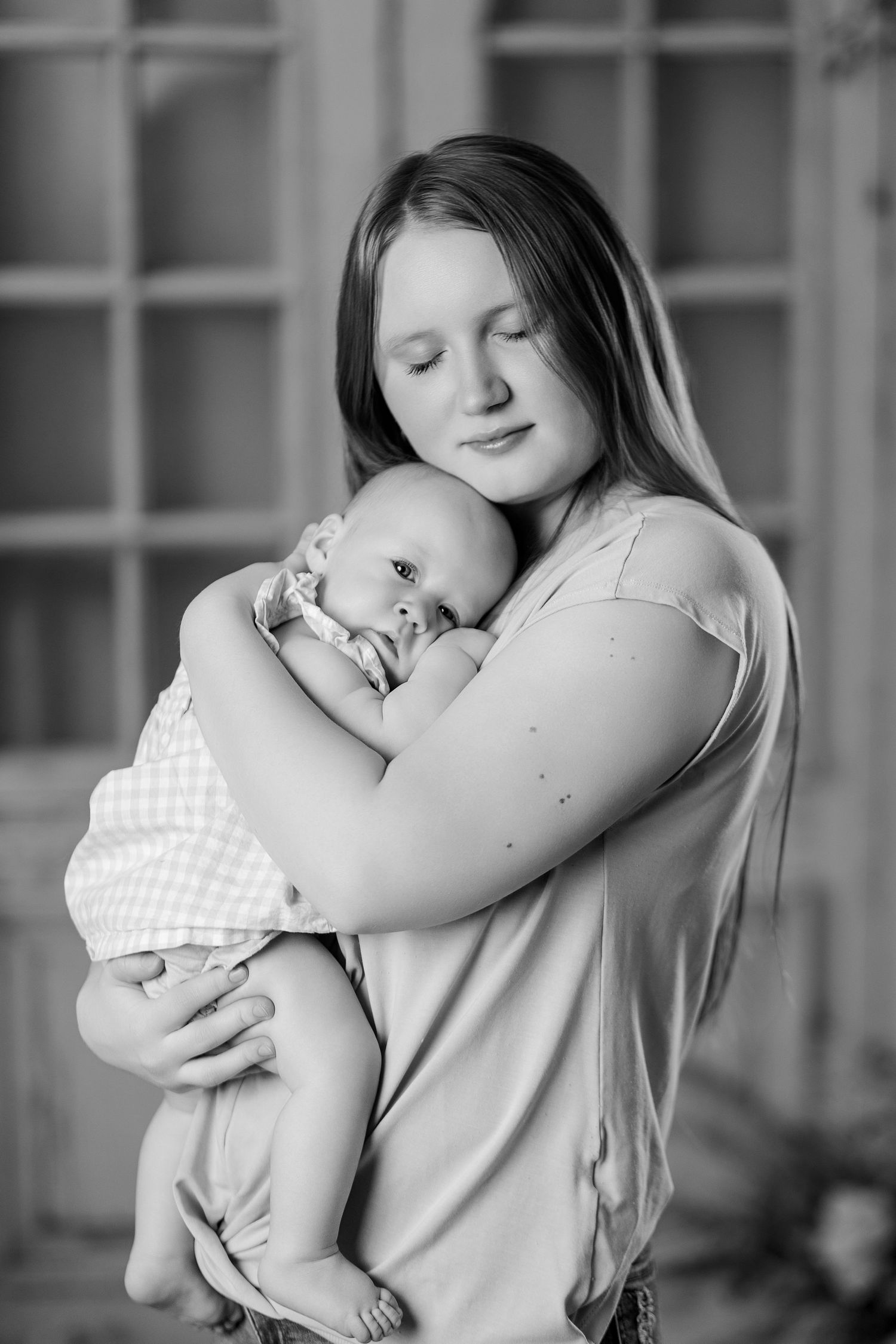 Tender black and white portrait of a young mother with long hair lovingly embracing her sleeping newborn.