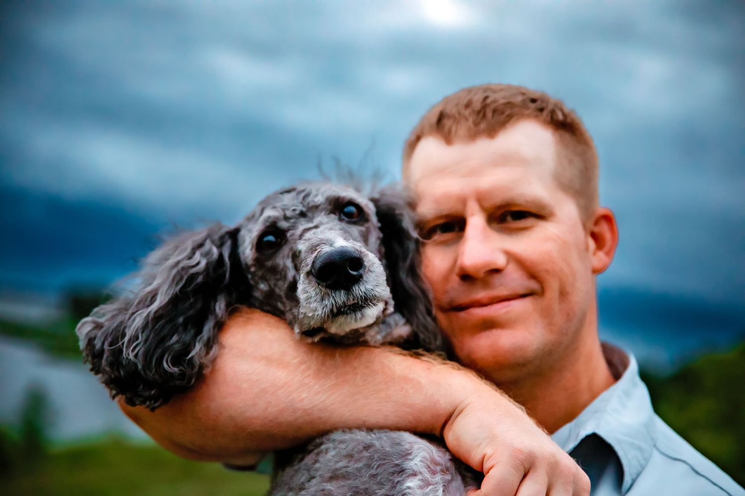 An affectionate moment captured outdoors with a dramatic cloudy sky background.
