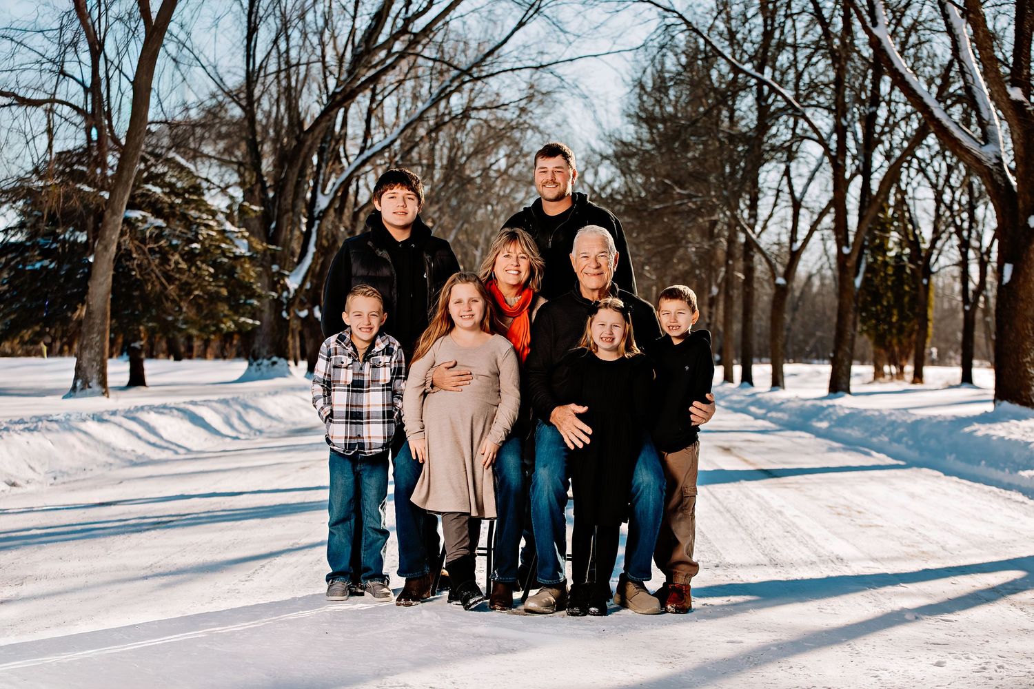 A family group poses together on a snow-covered path with bare trees in the background.