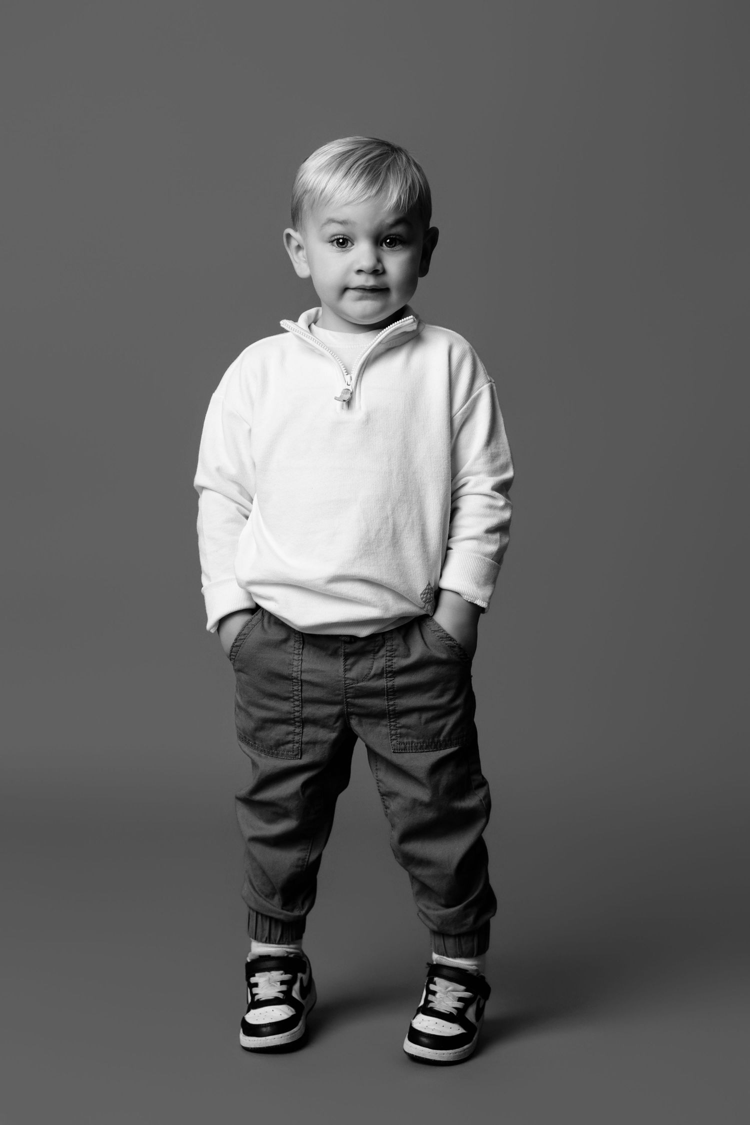 A child models casual wear with brown pants and white sweater in a studio setting.