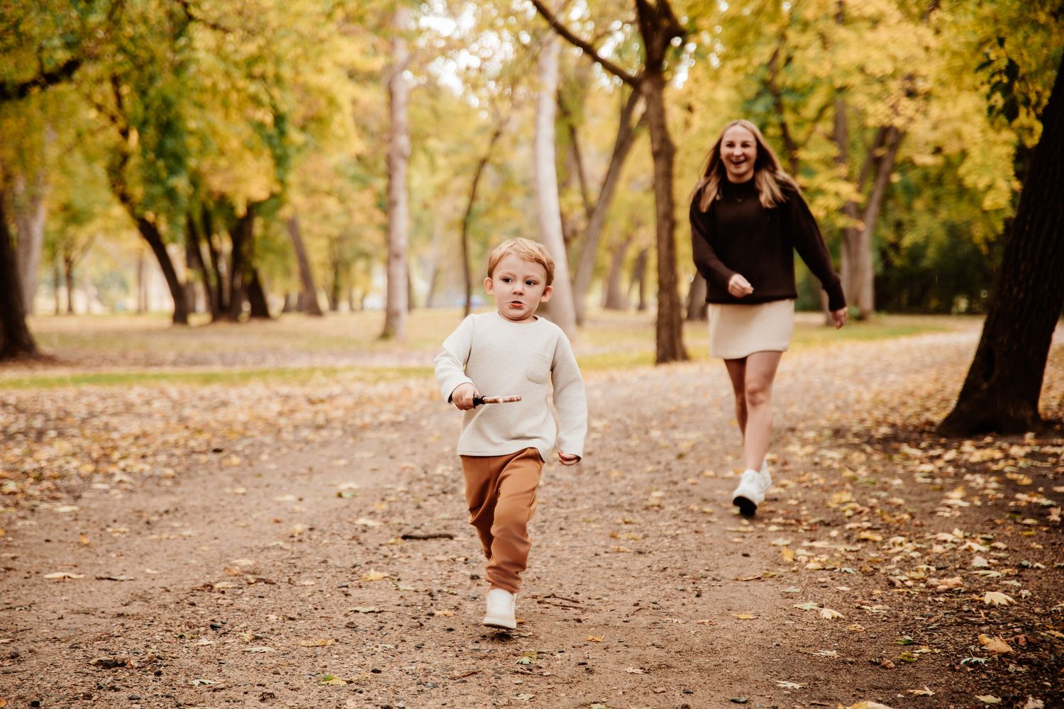 Family walking together on fallen leaves in autumn park setting.