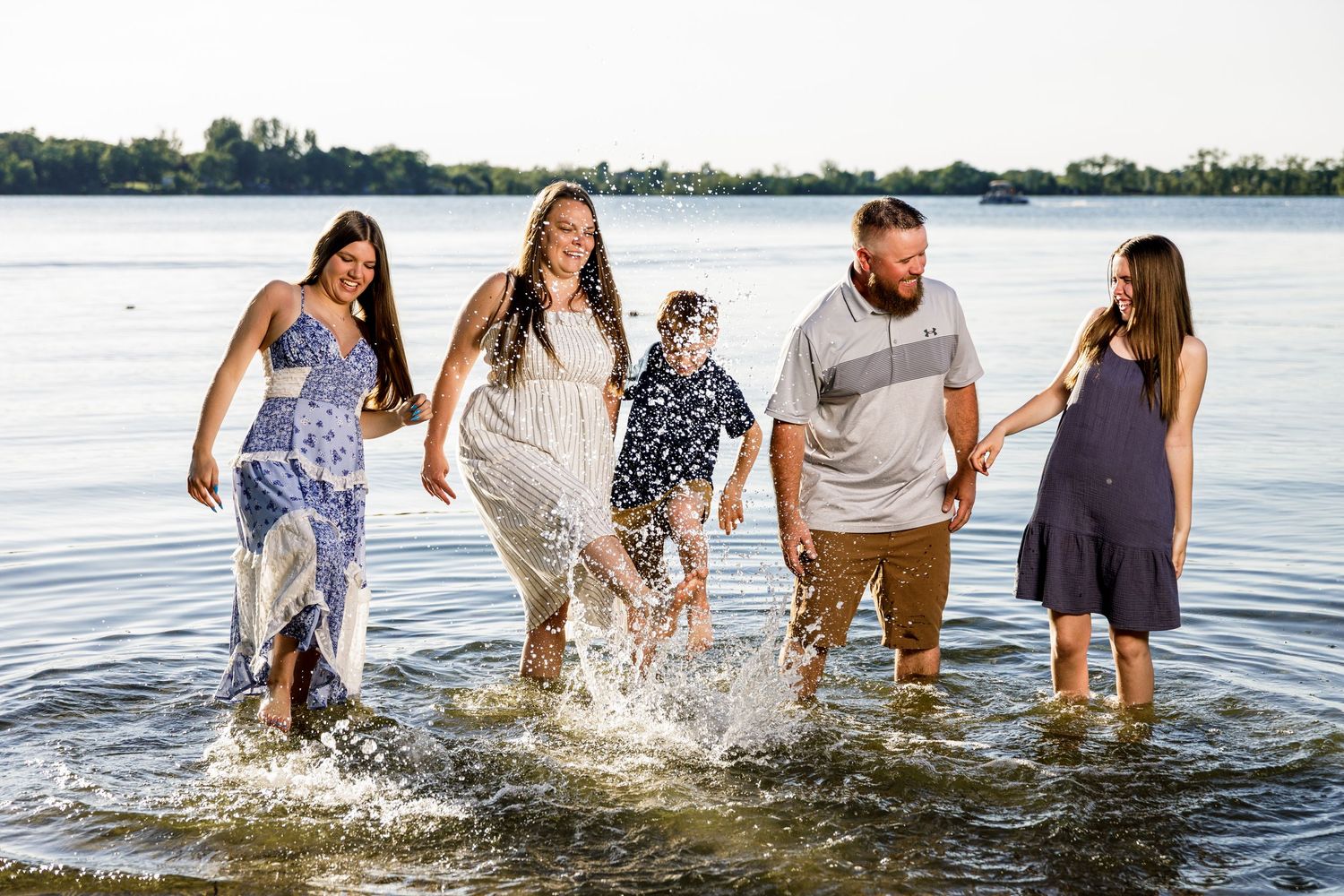 Joyful family of five splashing and walking through a lake in the golden evening light.