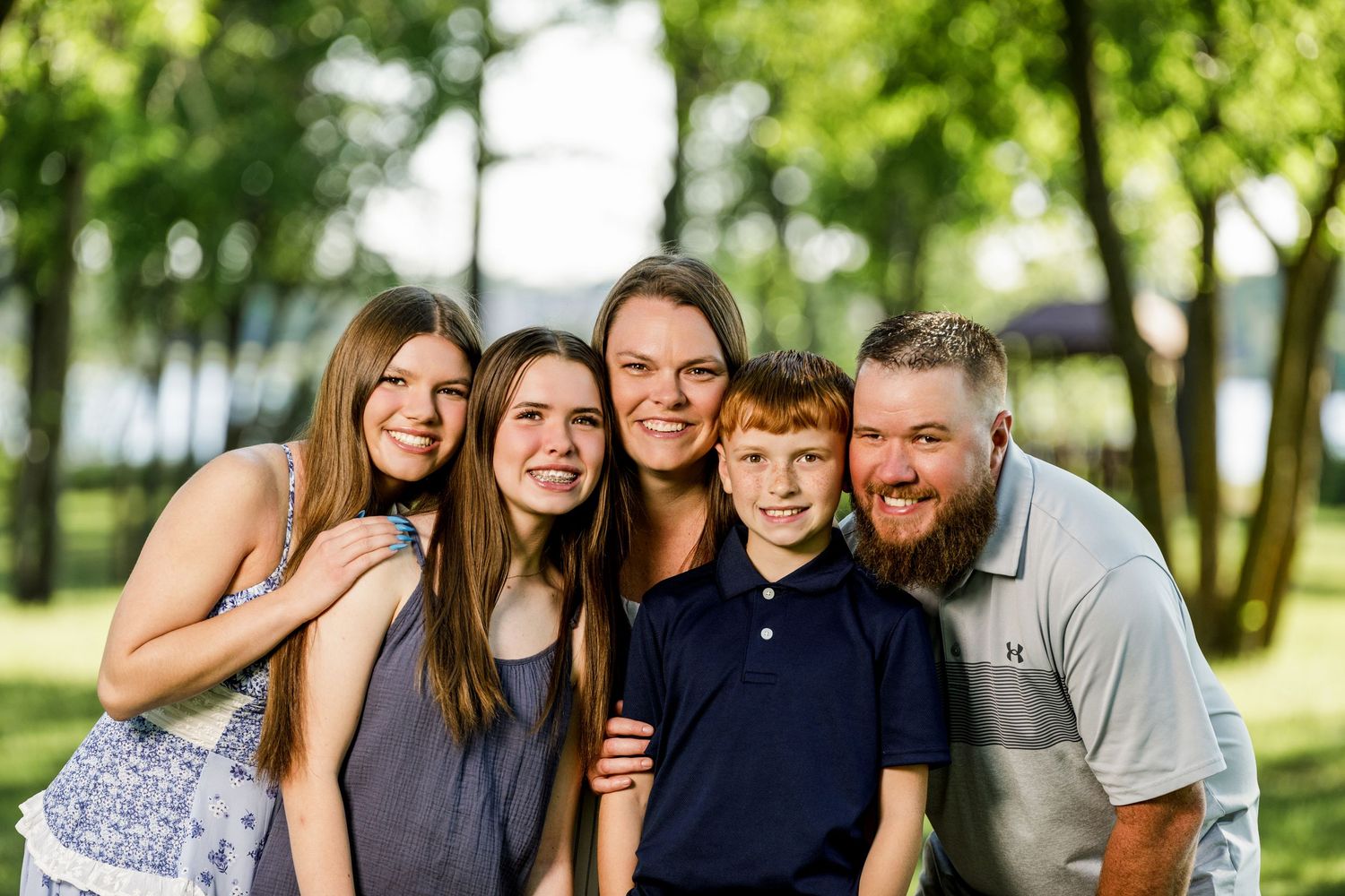 Happy family of five smiling outdoors in a lush green park setting for a summer portrait photo.