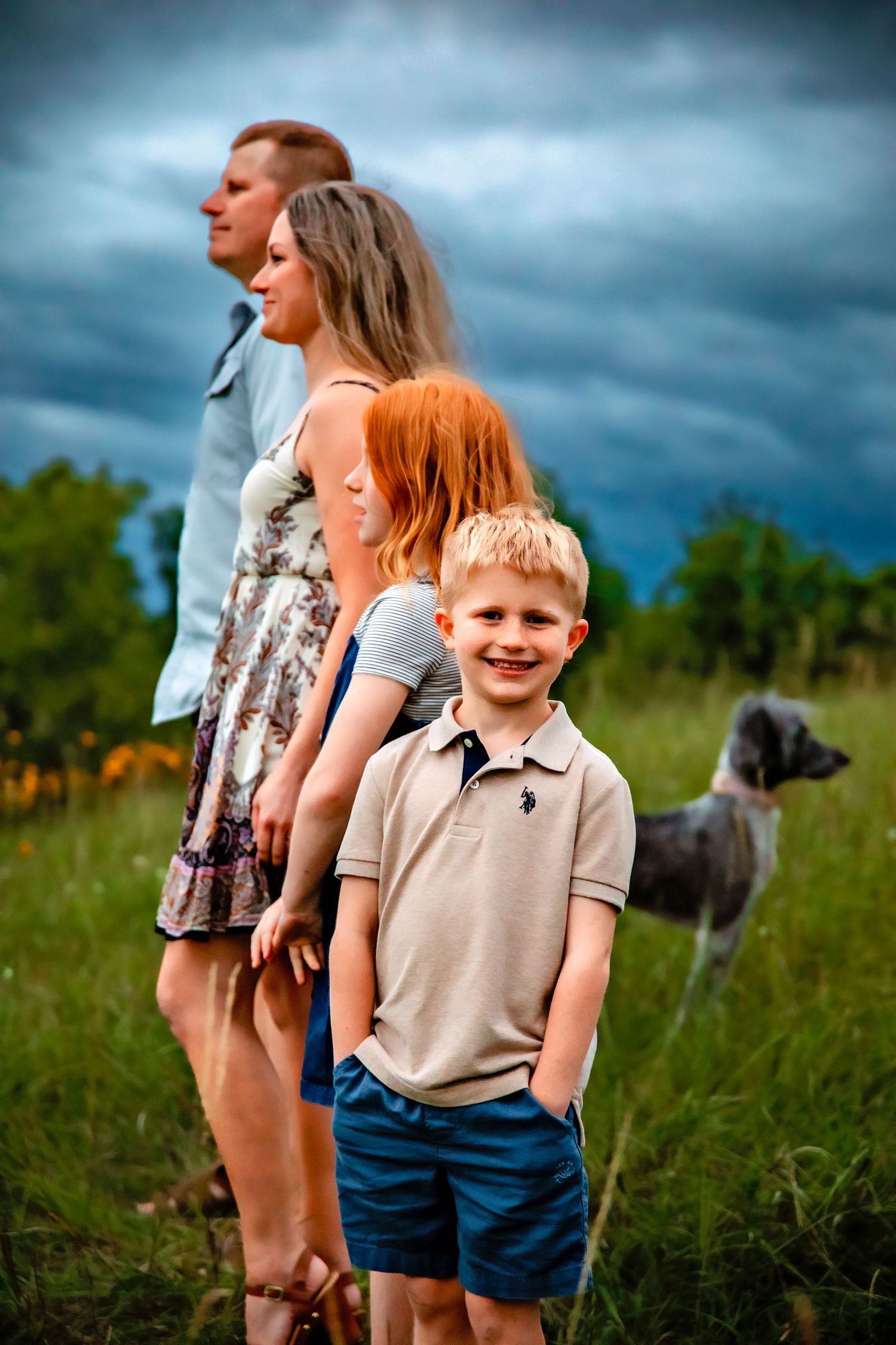 Family and their dog pose together in a field under dramatic stormy skies.