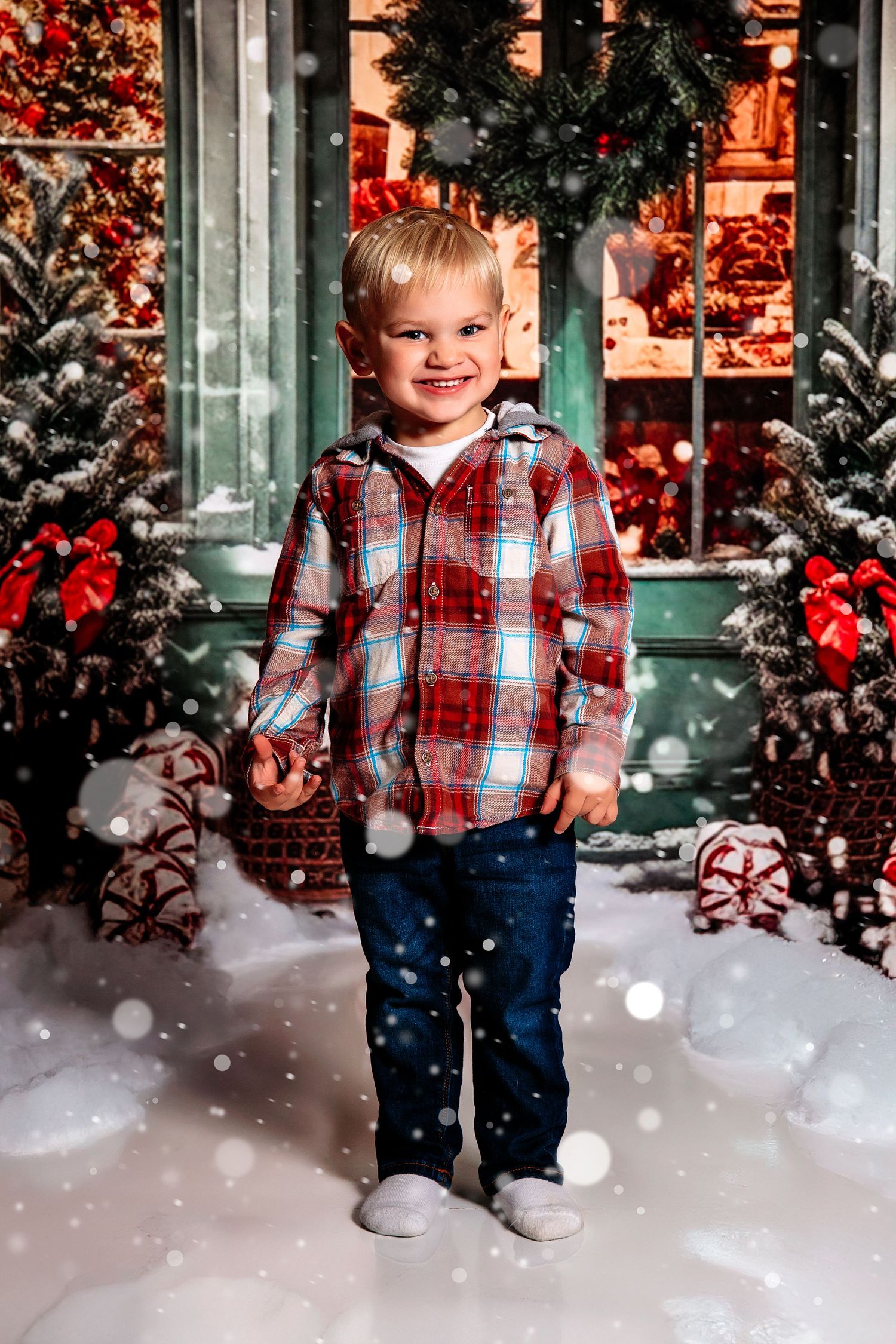 Festive outdoor portrait with snow, Christmas decorations, and plaid shirt against storefront.