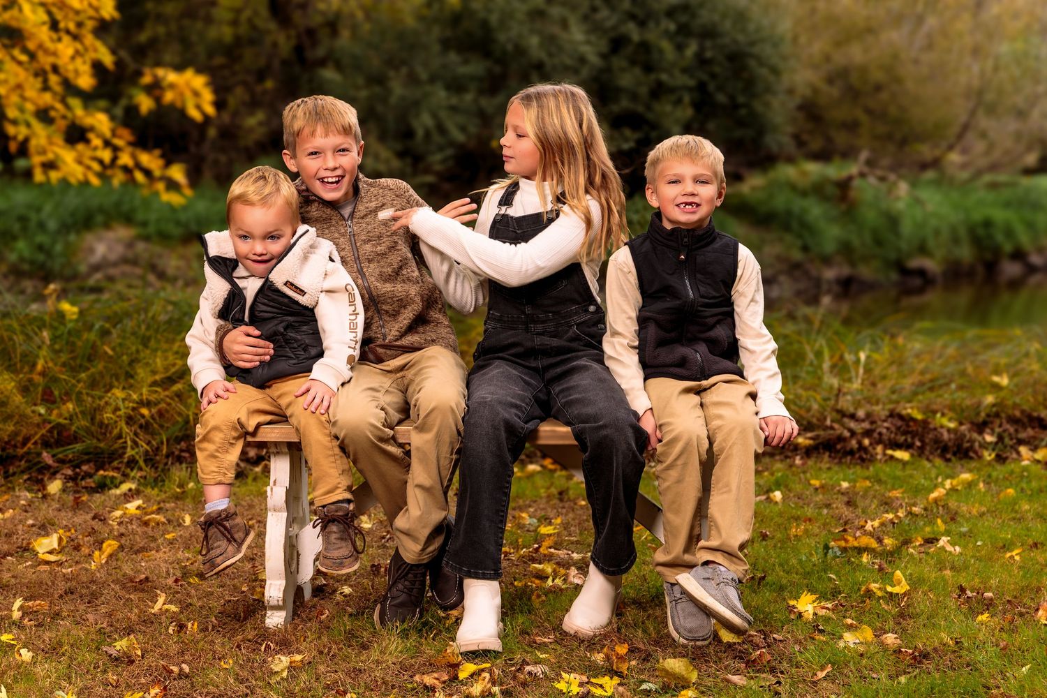 Family members sit casually on fallen leaves in an autumn outdoor setting wearing coordinated outfits.
