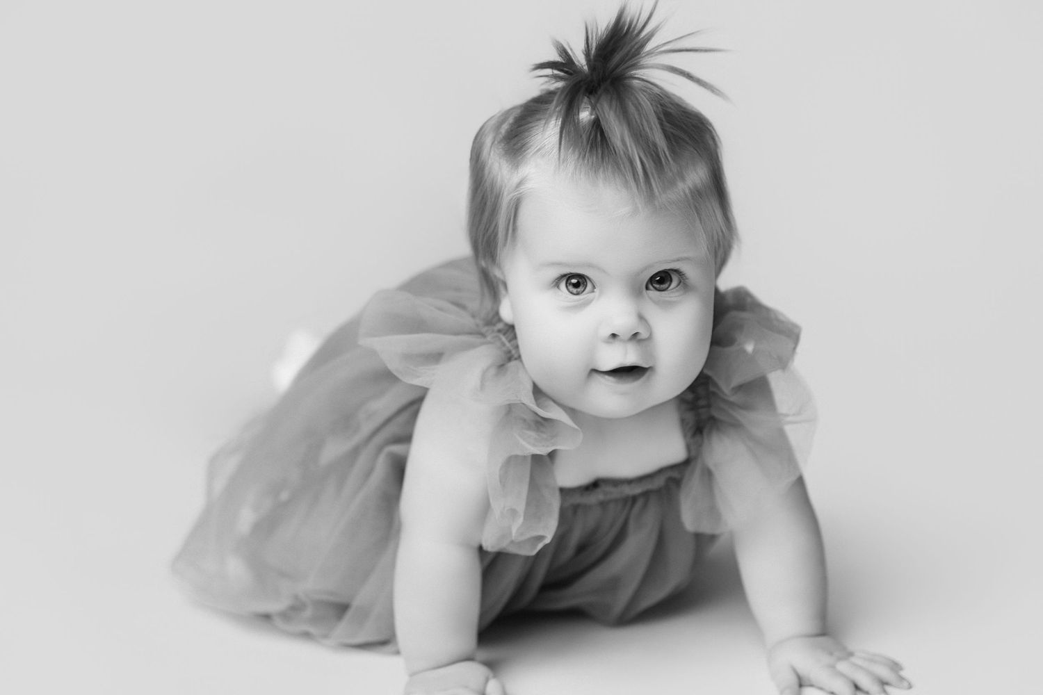 Baby in gray tulle dress crawling on white studio backdrop.
