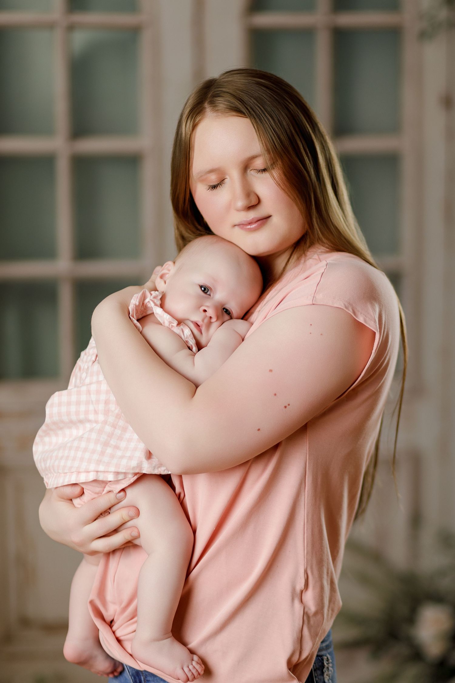 Tender moment as young mother in pink top gently cradles sleeping newborn baby to her chest.