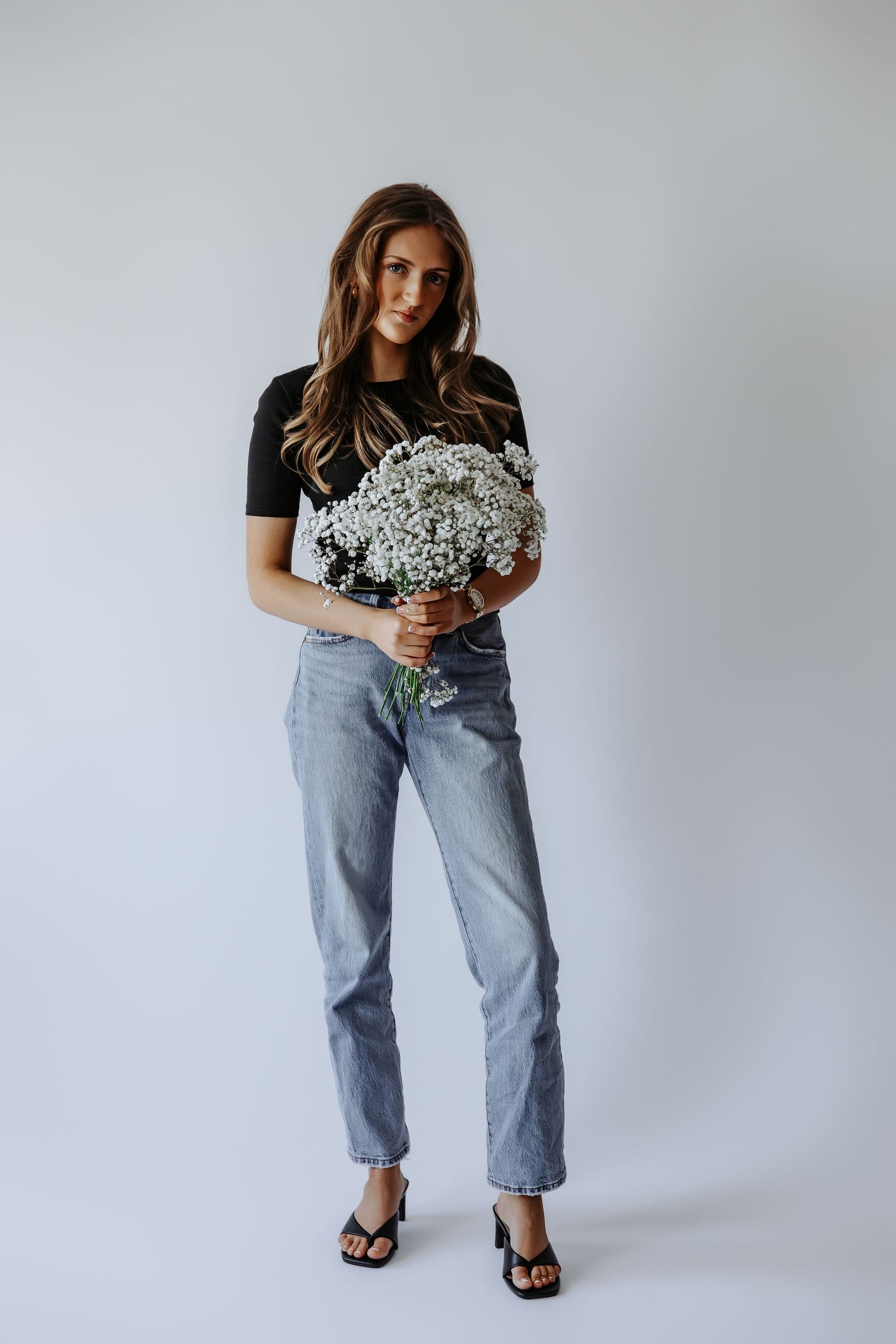 Young woman standing holding large bouquet of white baby's breath, black tee and jeans.
