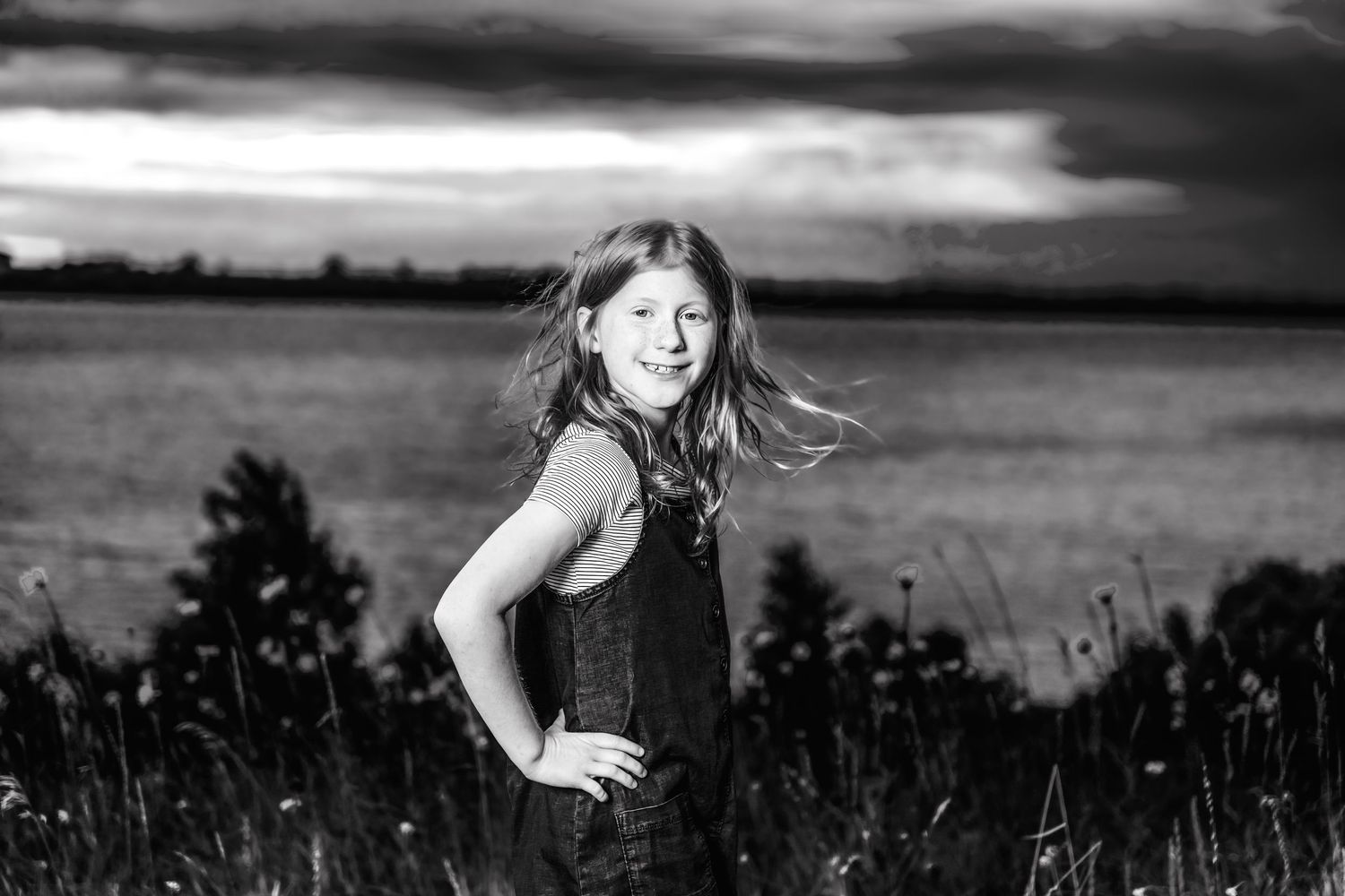 A candid portrait at sunset shows a playful pose against a dramatic sky and tall grass.