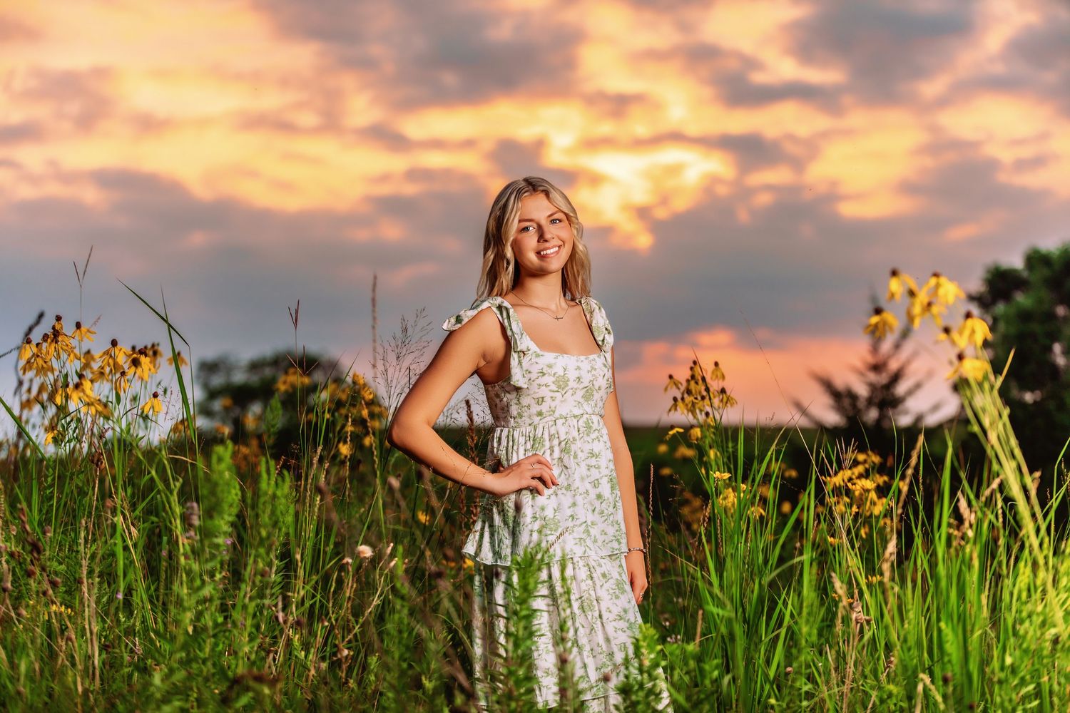 Young woman in floral dress standing in wildflower field at golden sunset.