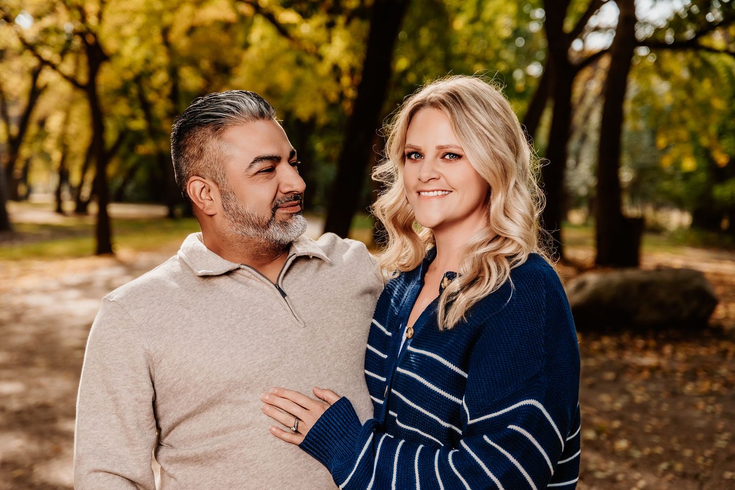 Couple in casual attire sharing romantic moments during an autumn photoshoot in a park with fallen leaves.